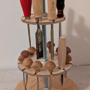 May include: A wooden tool holder with a rotating base. The holder features a variety of wood carving tools with wooden handles. The tools are arranged in a circle around the base. The base is made of plywood and has a natural wood finish.