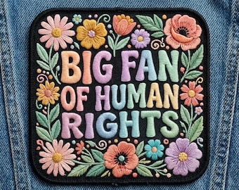 Może przedstawiać: Haftowana naszywka z napisem "BIG FAN OF HUMAN RIGHTS" w kolorowych, wypukłych literach. Naszywka jest czarna z kwiatowym obramowaniem z różowymi, pomarańczowymi, żółtymi i fioletowymi kwiatami z zielonymi liśćmi. Naszywka jest kwadratowa z zaokrąglonymi rogami.