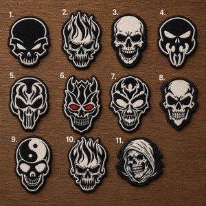 May include: A collection of eleven embroidered patches featuring various skull designs in black and white thread. Each patch is numbered from one to eleven, showcasing distinct artistic interpretations of skulls, including flaming, hooded, and yin-yang motifs.