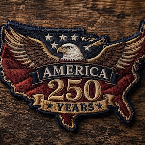 May include: Embroidered patch in the shape of the United States, featuring an eagle with outstretched wings. The patch is in red, white, blue, and gold, with the text "AMERICA 250 YEARS". The patch is on a wooden surface.