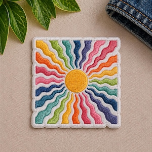 May include: Embroidered patch featuring a vibrant sunburst design. The sun's center is a bright yellow circle, with colorful, wavy rays in shades of orange, pink, green, blue, and purple. The patch has a white border and is square-shaped.
