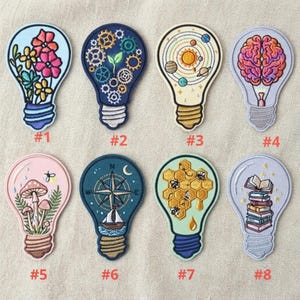 May include: Eight embroidered iron-on patches shaped like light bulbs, each featuring unique designs: flowers, gears, a solar system, a brain, mushrooms, a compass with a sailboat, a honeycomb with bees, and a stack of books.