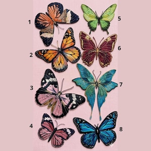 May include: Eight embroidered butterfly patches in a range of colours, such as orange, blue, green, and pink. Each butterfly features intricate wing patterns, set against a soft pink backdrop. These patches are suitable for adding decoration to clothing or accessories.