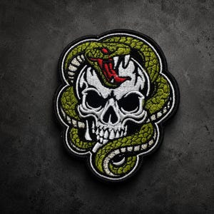 May include: An embroidered patch featuring a white human skull with black eye sockets and nasal cavity, encircled by a green snake with a red mouth and white fangs. The design is outlined in black thread with a thick black border.