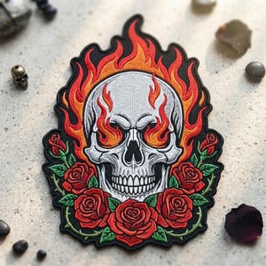 May include: An embroidered patch featuring a white skull centered within vibrant orange and red flames. The skull is framed at the bottom by a cluster of detailed red roses with green leaves and thorny stems, all set against a black background.