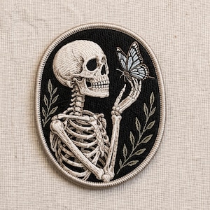 May include: Embroidered patch featuring a detailed skeleton holding a butterfly. The skeleton is cream-colored, set against a black oval background with a silver border. The butterfly has blue and white wings, and the design includes green leaves.