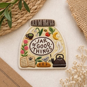 May include: Embroidered patch in the shape of a jar, with the words "JAR OF GOOD THINGS" in a central oval. The patch features illustrations of a teacup, flowers, a bee, a bird, and a teapot. The color palette includes beige, brown, yellow, and green.