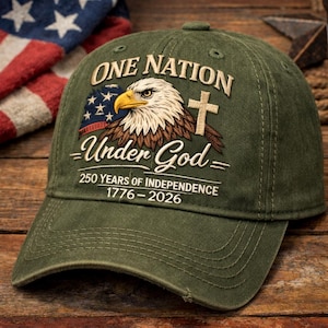 May include: An olive green baseball cap featuring an embroidered bald eagle, a cross, and an American flag segment. The text reads: ONE NATION Under God, 250 YEARS OF INDEPENDENCE, 1776-2026. The cap has a distressed brim and structured crown.
