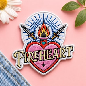May include: Embroidered patch with a heart, flame, and sword design. The patch features a pink heart with the word "FIREHEART" in white lettering. Two swords are crossed behind the heart, and a flame sits atop the heart. The patch is outlined in white.