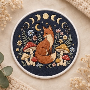 May include: Embroidered patch with a fox, mushrooms, flowers, and moon phases on a navy blue background. The fox is brown and cream, with detailed stitching. The patch has a white border and is for clothing or accessories.