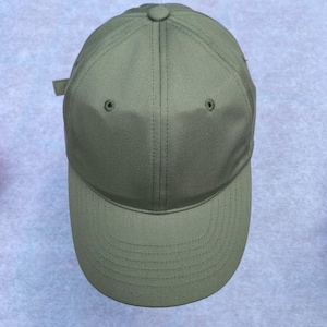 May include: Olive green baseball cap with a curved brim. The cap features a button on top and two small ventilation holes. A fabric strap is visible on the back for adjustment. The cap is made of a durable, solid-colored fabric.