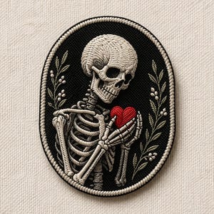 May include: Embroidered patch featuring a skeleton holding a red heart. The skeleton is white, set against a black oval background, framed by a white rope-like border and sprigs of leaves. A unique gothic-themed patch.