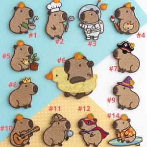 May include: A collection of embroidered patches featuring capybaras in various costumes. Designs include a chef, astronaut, pirate, and superhero. Each patch has a small orange fruit on its head.