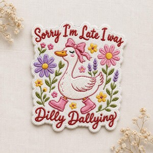 May include: An embroidered patch featuring a white goose wearing a pink bow and pink boots, surrounded by colorful flowers. The text reads Sorry I'm Late I was Dilly Dallying in red thread. The patch has a scalloped edge and a white background.