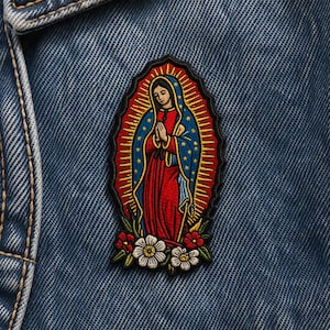 Peut inclure: Écusson brodé représentant la Vierge Marie en robe rouge et bleue, avec une auréole dorée et des motifs floraux. L'écusson est cousu sur une veste en jean bleue, mettant en valeur son design et ses couleurs.