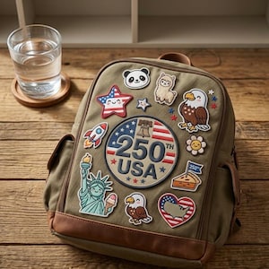 May include: An olive green backpack with brown leather accents, adorned with colorful embroidered patches. Patches include a panda, an eagle, a star, a rocket, and a patch that says "250th USA". A glass of water sits on a wooden coaster.