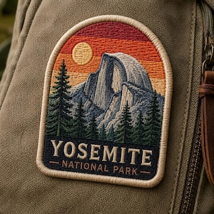May include: Embroidered patch depicting a Yosemite National Park scene. The design shows a mountain, trees, and a sunset. The text "YOSEMITE NATIONAL PARK" is at the bottom. The patch is attached to a green canvas backpack.