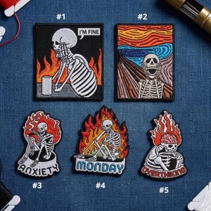 May include: Set of five embroidered patches with skeleton designs. One patch features a skeleton with the text "I'M FINE". Other patches include the words "ANXIETY", "MONDAY", and "OVERTHINKING". Each patch has a black border and colorful flames.