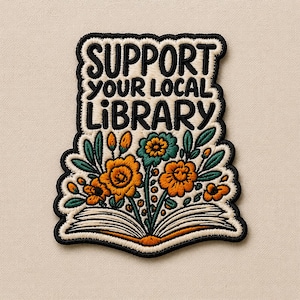 May include: Embroidered patch with the text "SUPPORT YOUR LOCAL LIBRARY" in black letters on a cream background. The patch features orange and teal flowers blooming from an open book, with green leaves and a black border.