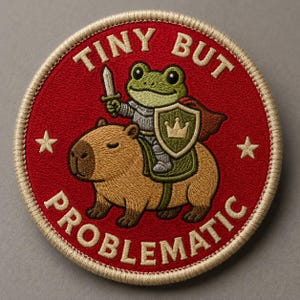 May include: Embroidered patch with a red background and a tan border. The patch features a frog knight riding a capybara, holding a sword and shield. Text on the patch reads "TINY BUT PROBLEMATIC" with two white stars.