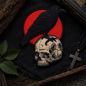 May include: Embroidered patch featuring a black raven with red eyes perched atop a skull. The raven and skull are detailed with tan and black thread, set against a red circle and black background. A gothic-themed accessory.