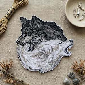 May include: Embroidered patch featuring two wolves, one black and one white, intertwined in a yin-yang design. The black wolf has amber eyes. The white wolf is howling. The patch is on a neutral-toned fabric.