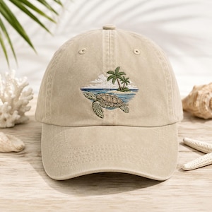May include: Tan baseball cap with an embroidered design of a sea turtle, palm trees, and ocean waves. The cap has a curved brim and a fabric strap closure. The design features shades of green, blue, and brown.