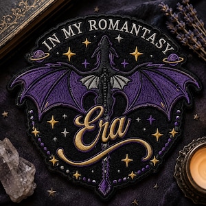 May include: Embroidered patch with a black background, featuring a purple dragon with outstretched wings. The text "IN MY ROMANTASY Era" is in gold script. Gold and purple stars and planets surround the dragon, creating a fantasy theme.