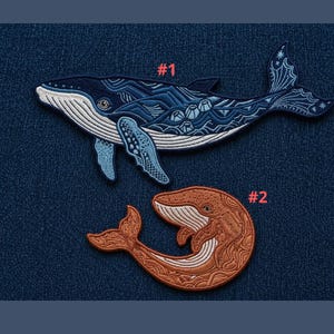 May include: Two embroidered whale patches. The top whale is blue with white accents and the text "#1". The bottom whale is brown with white accents and the text "#2". Both patches are on a blue background.
