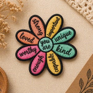 May include: Embroidered daisy patch with colorful petals and the words "strong," "important," "unique," "kind," "capable," "enough," "worthy," and "loved." The center of the flower reads "you are." The patch has a black border.