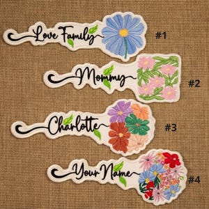 May include: Embroidered patches in a key shape with floral designs and text. The patches include the phrases "Love Family", "Mommy", "Charlotte", and "Your Name". Each patch has a white background with black script.