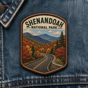 May include: Embroidered patch featuring a scenic view of Shenandoah National Park. The design includes a winding road through a colorful autumn landscape with mountains and the text "SHENANDOAH NATIONAL PARK". The patch is set against a denim background.