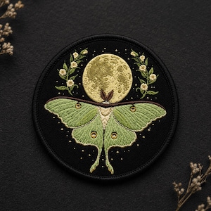 May include: Embroidered patch featuring a green luna moth with detailed wing patterns, set against a black background. A full moon and floral accents complete the design. The patch is round and suitable for clothing or accessories.