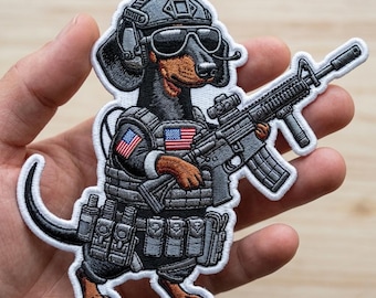 May include: Embroidered patch featuring a dachshund dog in military gear, including a helmet, sunglasses, and tactical vest with American flag patches. The dog is holding a rifle. The patch has a white border.