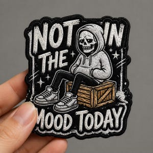 May include: Black embroidered patch featuring a cartoon skeleton in a hoodie sitting on a wooden crate. The text "NOT IN THE MOOD TODAY" is in white, stylized lettering. The patch has a black border and a gray background.