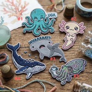 May include: Embroidered patches featuring sea creatures: an octopus with "UGH" text, an axolotl, a shark and hammerhead, a whale, and a squid holding a coffee cup. Each patch has detailed stitching and vibrant colors, perfect for jackets or bags.