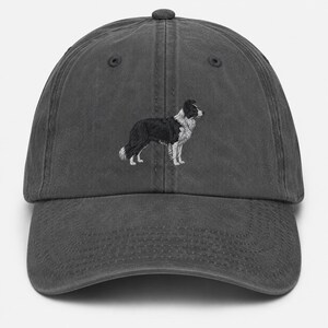 May include: A charcoal gray baseball cap featuring an embroidered image of a Border Collie dog in black and white. The cap has a curved brim and an adjustable strap.