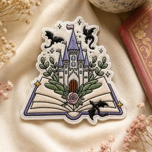May include: Embroidered patch depicting a fairytale castle with purple turrets, set within an open book design. The patch features black bats, a pink rose, and green foliage, with a purple border and star accents.