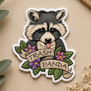 May include: Embroidered patch featuring a raccoon with black and tan fur, a pink tongue, and the words "Trash Panda" on a banner. The patch is surrounded by green leaves and purple and pink flowers.
