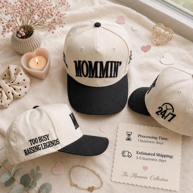 May include: Cream-colored baseball caps with black visors. One cap has "MOMMIN'" embroidered across the front, another says "TOO BUSY RAISING LEGENDS", and a third displays "24/7". The caps are part of "The Mommin' Collection".