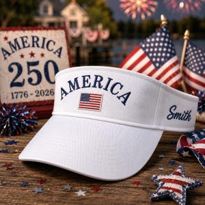 May include: A white visor featuring the word AMERICA embroidered in navy blue thread above a small rectangular American flag patch. The name Smith is embroidered in navy blue script on the side of the visor. The visor has a curved brim.