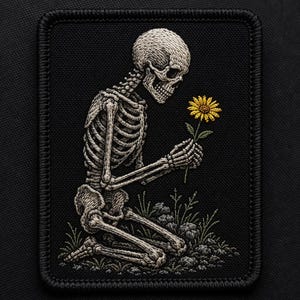 May include: Embroidered patch featuring a kneeling skeleton holding a yellow daisy. The skeleton is detailed in shades of gray and white, set against a black background. The patch includes a border and small patches of grass and rocks.