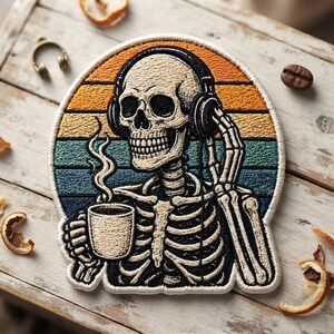 May include: A circular embroidered patch featuring a skeleton wearing black headphones while holding a steaming mug of coffee. The background displays horizontal stripes in shades of orange, yellow, teal, and dark blue, creating a sunset effect.