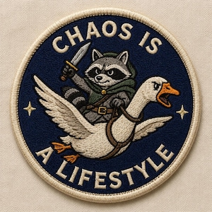 May include: Embroidered patch with a raccoon riding a goose, holding a knife. The patch is circular with the words "CHAOS IS A LIFESTYLE" in white lettering on a navy blue background. The raccoon wears a green cloak and the goose has a brown harness.