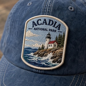 Peut inclure: Casquette de baseball bleue avec un écusson brodé « ACADIA NATIONAL PARK ». L'écusson représente un phare sur une côte rocheuse avec des vagues, des arbres et un ciel bleu. La casquette est en tissu doux et usé, idéale pour les activités en plein air.