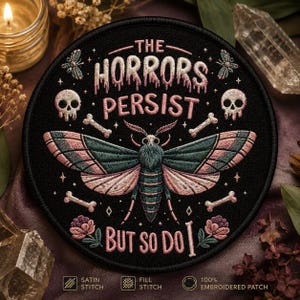 May include: Round black embroidered patch with the text "THE HORRORS PERSIST BUT SO DO I". The patch features a moth with teal and pink wings, skulls, bones, and floral accents. The patch is 100% embroidered.