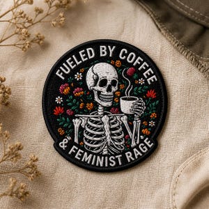 May include: Round black patch with white text that reads "Fueled by Coffee & Feminist Rage." The patch features a white skeleton holding a coffee cup, surrounded by colorful flowers. The design is embroidered.