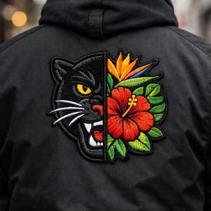 May include: Black jacket with a large embroidered patch. The patch is split down the middle, with a black panther on one side and a red hibiscus flower and tropical bird of paradise flower on the other.