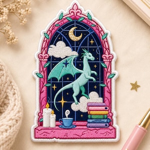 May include: Embroidered patch featuring a light blue dragon inside a stained-glass window design. The window includes a crescent moon, stars, clouds, and a stack of books. The patch has a pink border with green leaves.