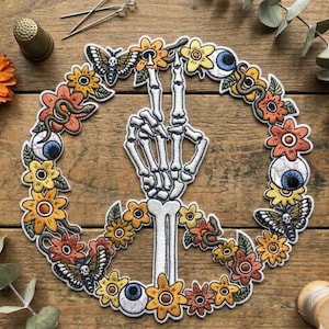 May include: Embroidered peace sign patch featuring a skeleton hand, surrounded by a wreath of flowers, butterflies, and eyeballs. The patch has a detailed design with orange, yellow, and blue accents, perfect for jackets, bags, or other fabric items.